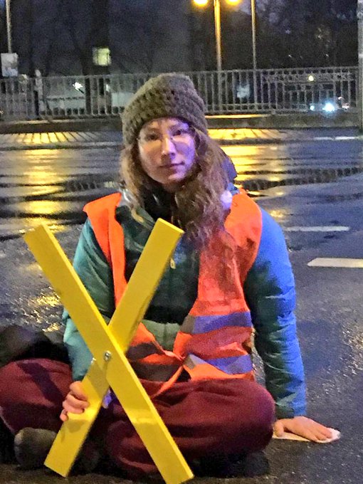 Eine Frau klebt auf einer nassen Straße. Sie hält ein gelbes X.