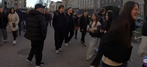 Ľudia prechádzajú mestskou ulicou s budovami v pozadí.
