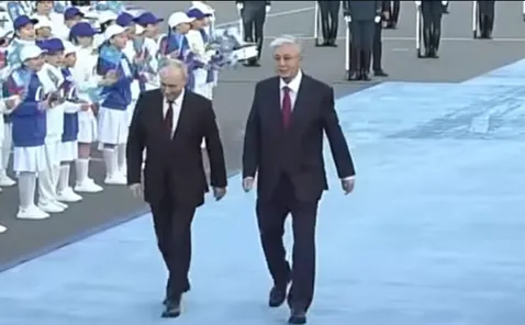 Putin a Tokayev kráčajú po modrom koberci, pozerajú deti.