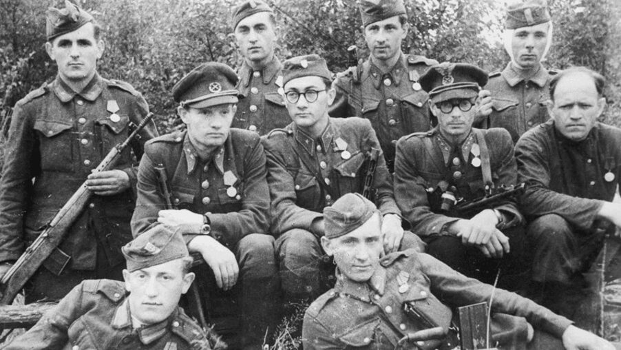 Čiernobiela fotografia skupiny vojákov v historických uniformách so zbraňami